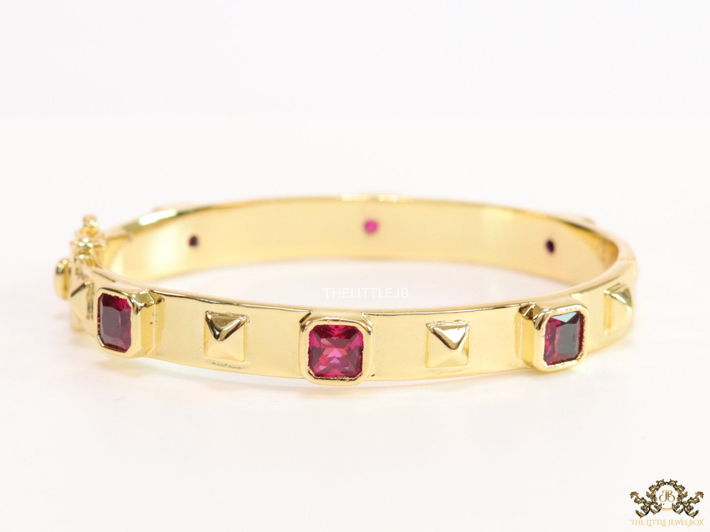 Band style bracelet in gold plating with gold plated details and ruby red colour stones
