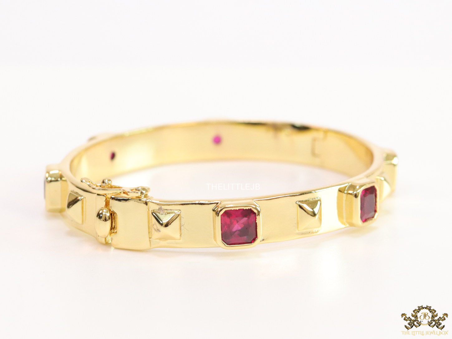 Band style bracelet in gold plating with gold plated details and ruby red colour stones