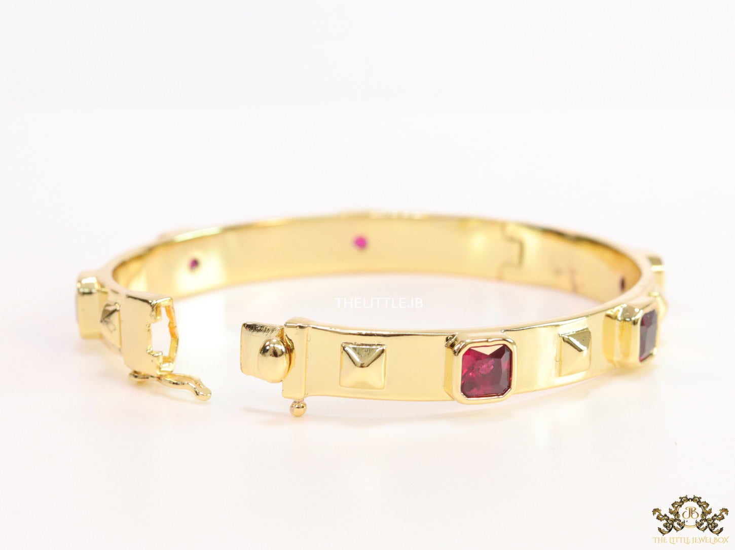 Band style bracelet in gold plating with gold plated details and ruby red colour stones