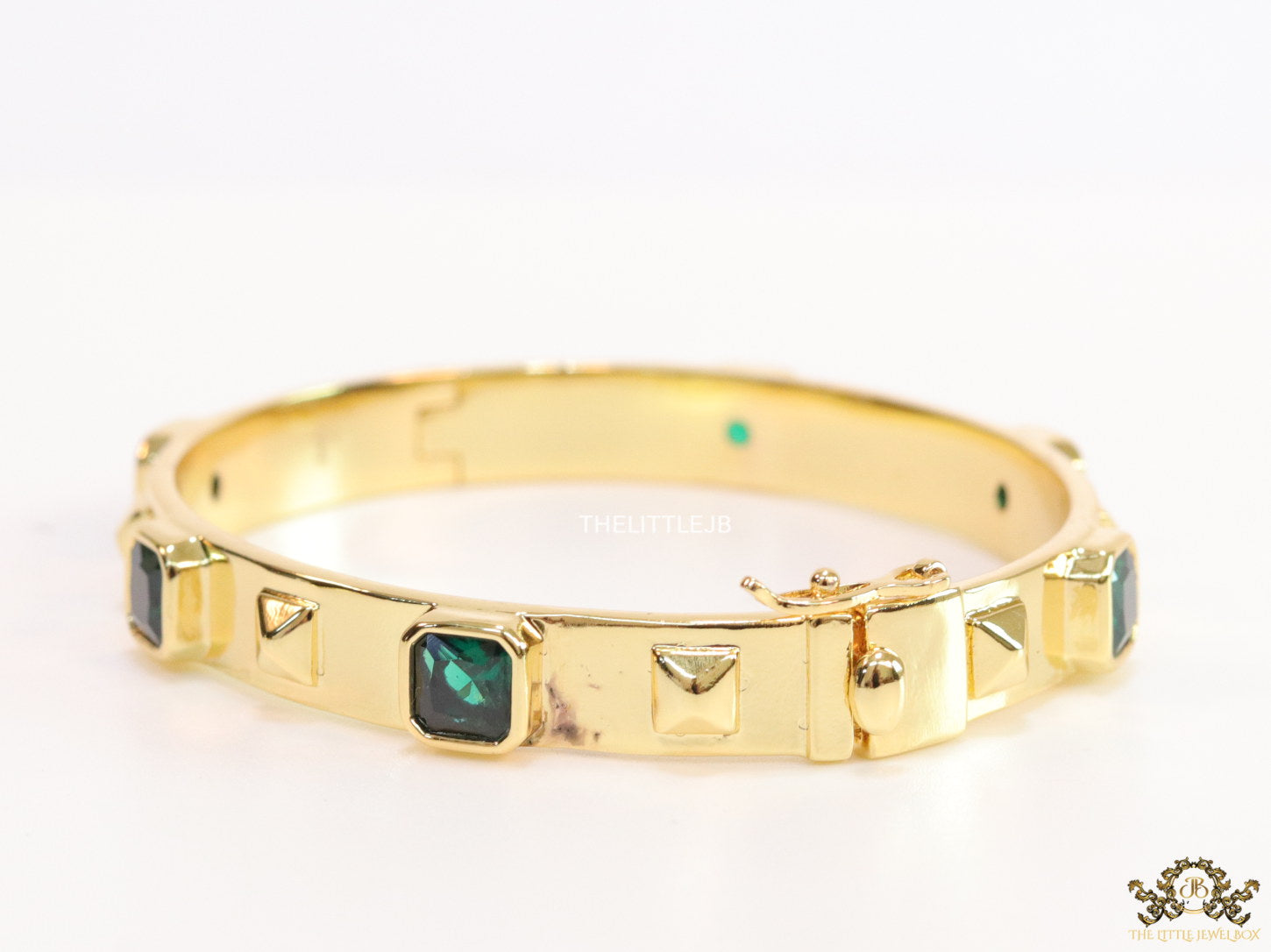 Band style bracelet in gold plating with gold plated details and emerald green colour stones
