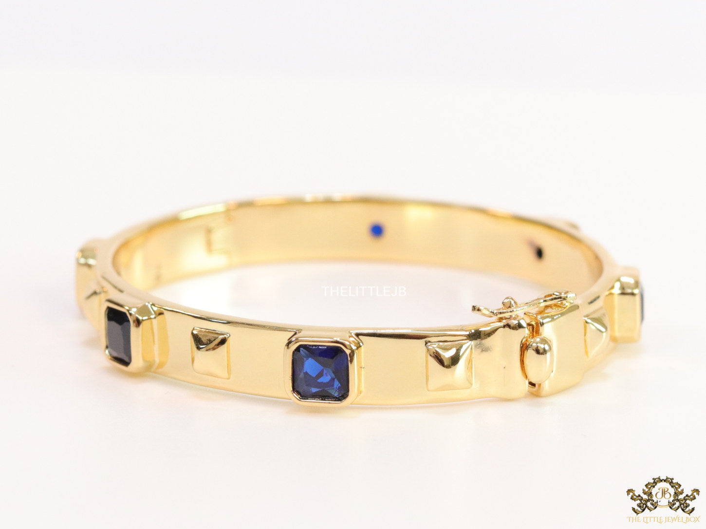 Band style bracelet in gold plating with gold plated details and sapphire blue colour stones