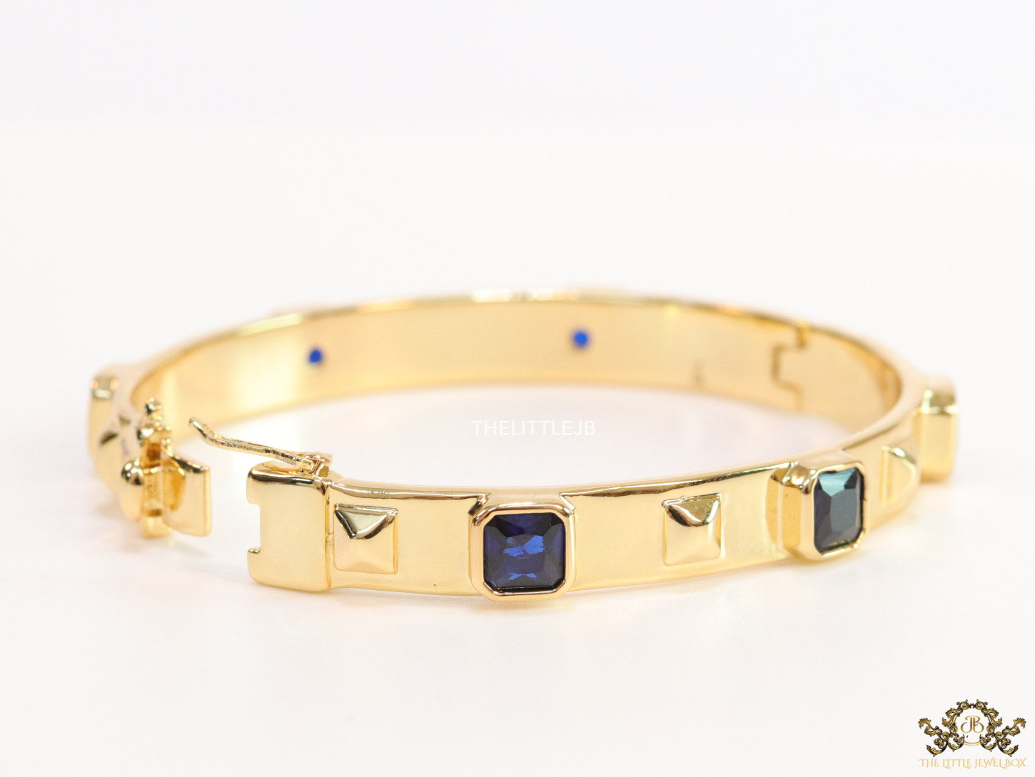 Band style bracelet in gold plating with gold plated details and sapphire blue colour stones