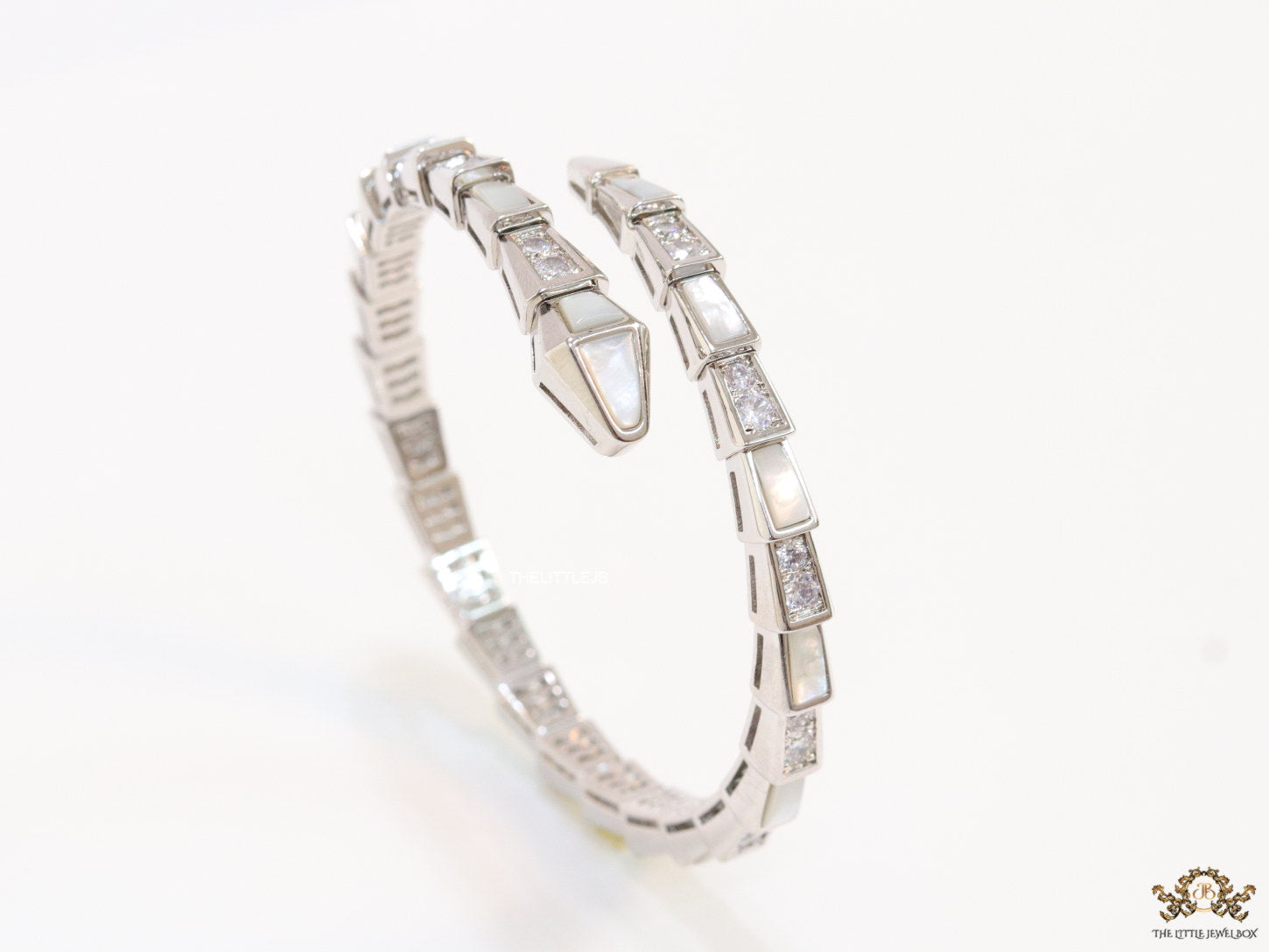 Open top platinum plated minimal serpentine bracelet with cubic zirconia stones and pearl white stones.