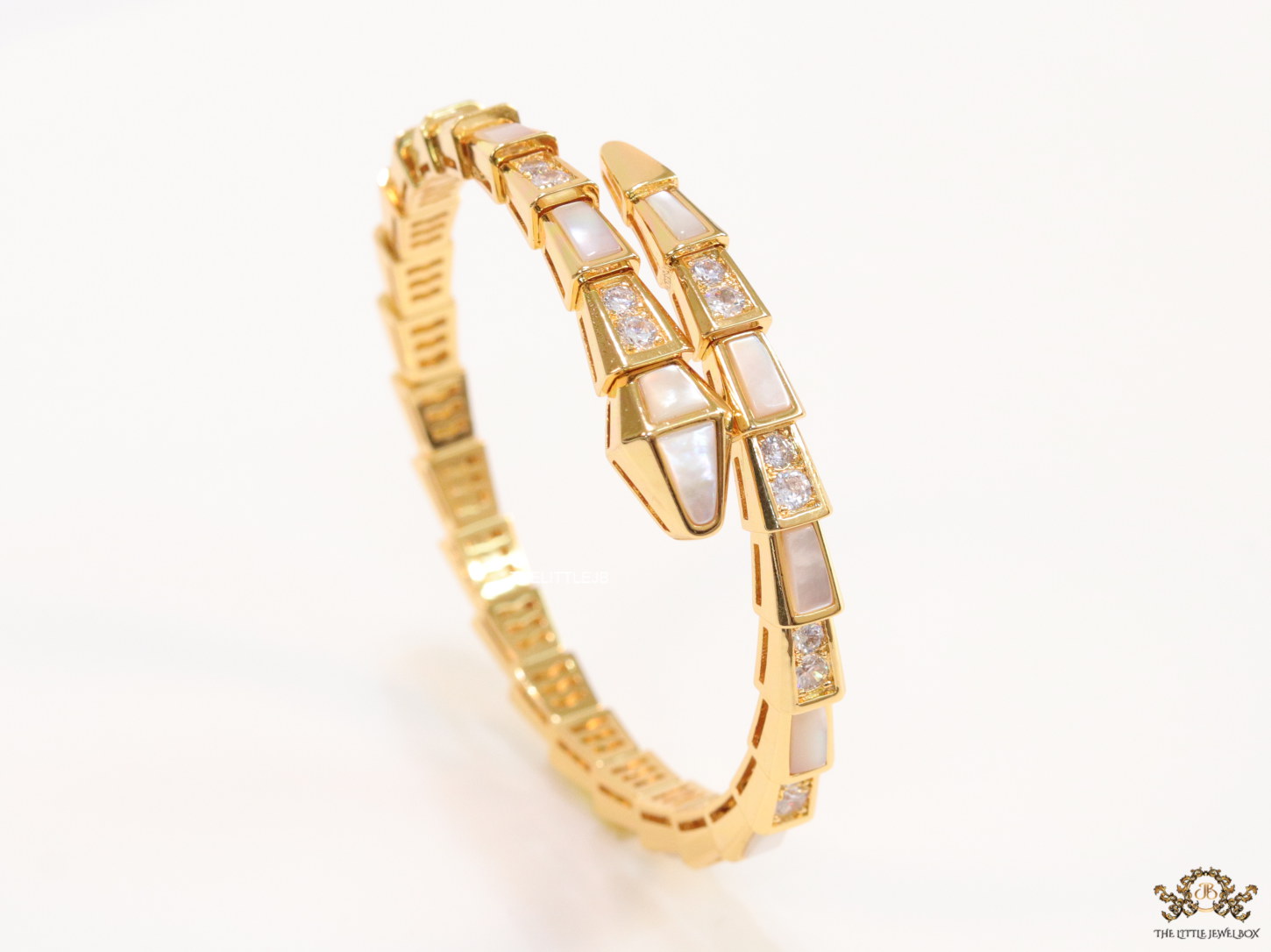 Open top gold plated minimal serpentine bracelet with cubic zirconia stones and pearl white stones.