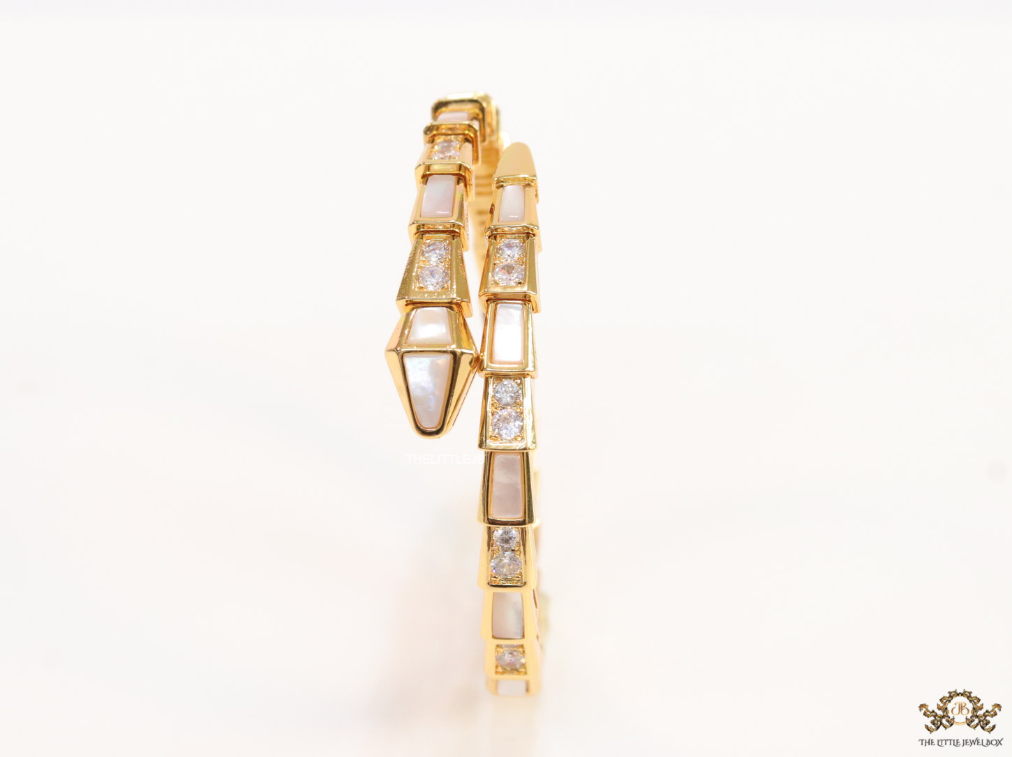Open top gold plated minimal serpentine bracelet with cubic zirconia stones and pearl white stones.