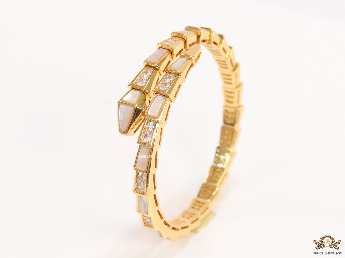 Open top gold plated minimal serpentine bracelet with cubic zirconia stones and pearl white stones.