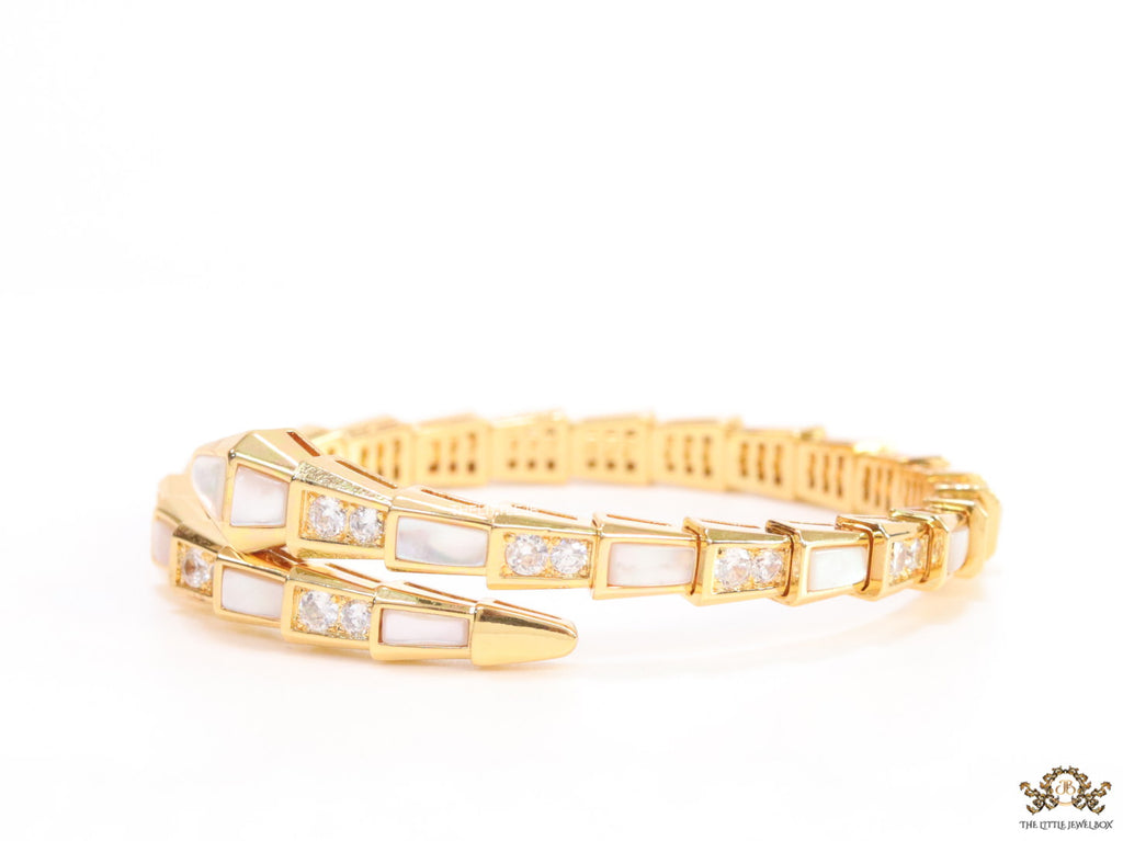 Open top gold plated minimal serpentine bracelet with cubic zirconia stones and pearl white stones.