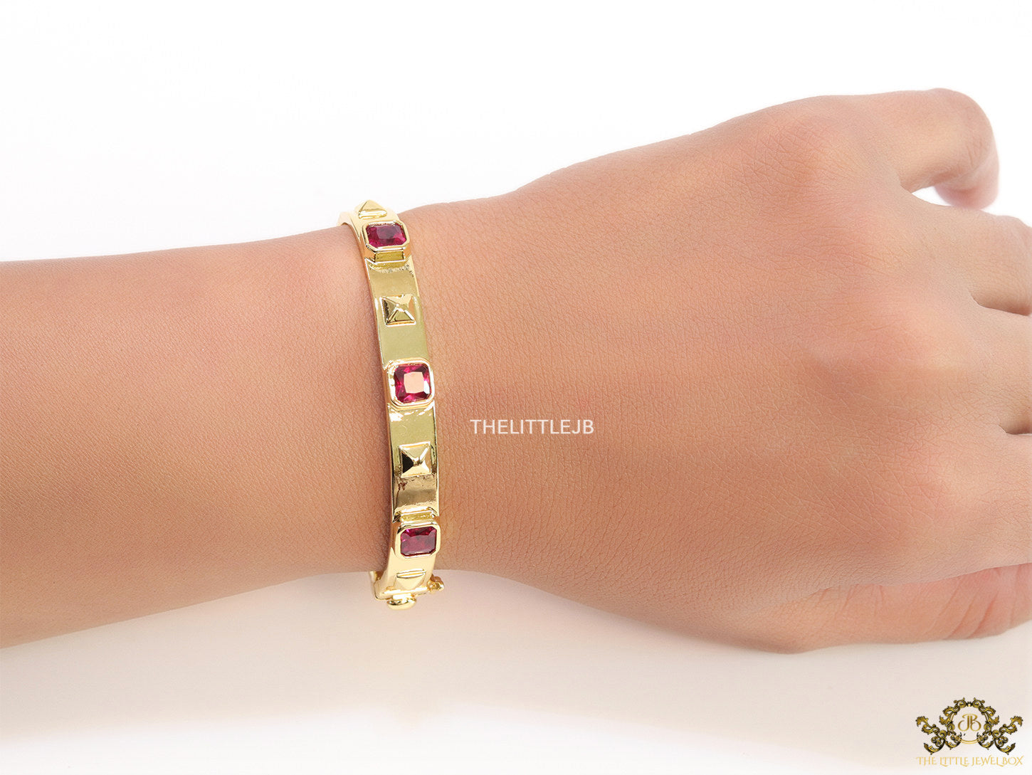 Band style bracelet in gold plating with gold plated details and ruby red colour stones