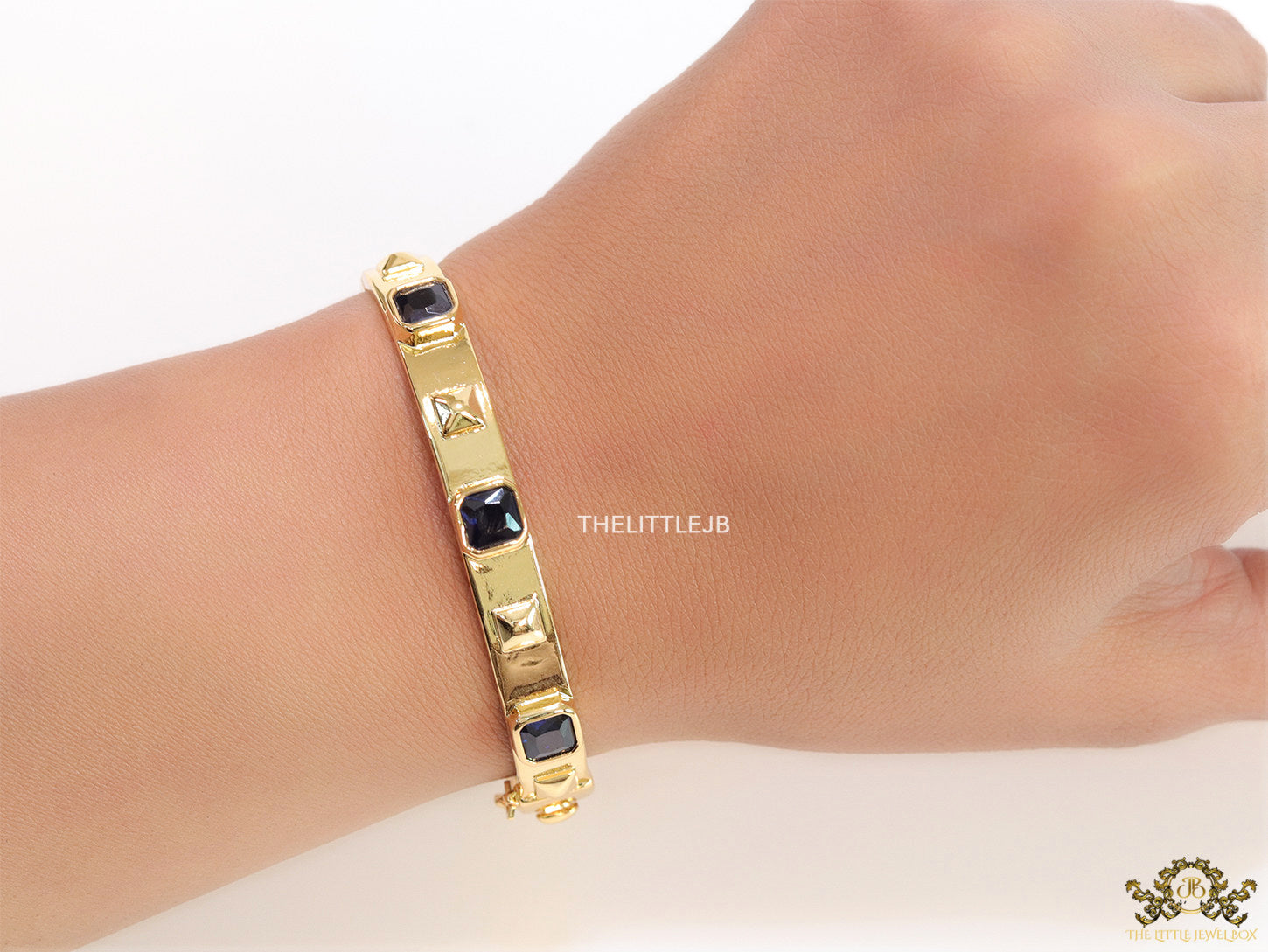 Band style bracelet in gold plating with gold plated details and sapphire blue colour stones