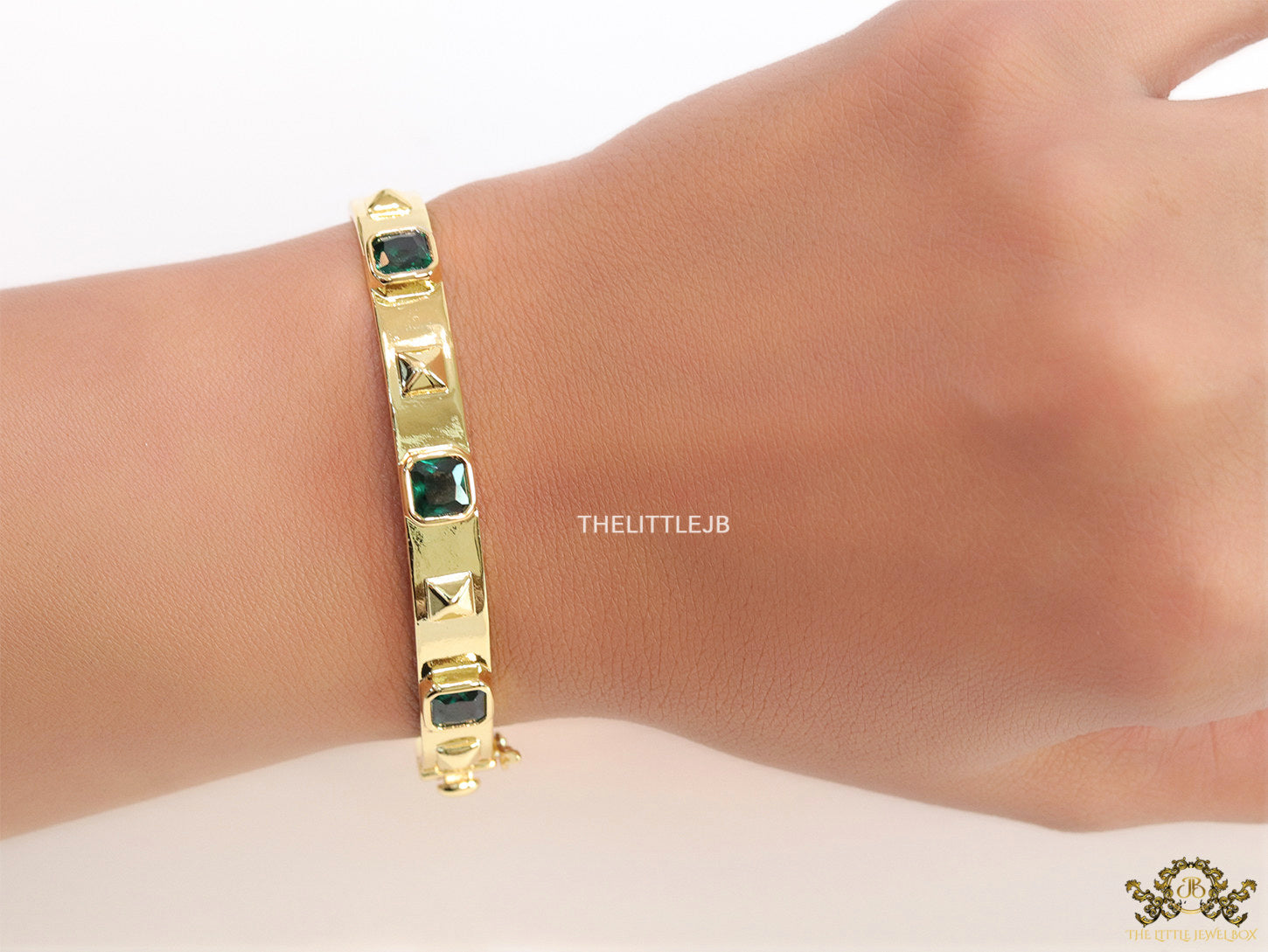 Band style bracelet in gold plating with gold plated details and emerald green colour stones