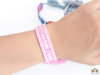 Adjustable pink woven bracelet with white knitted alphabets and tassels