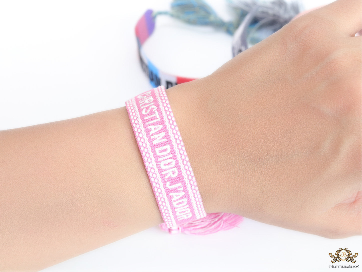 Adjustable pink woven bracelet with white knitted alphabets and tassels