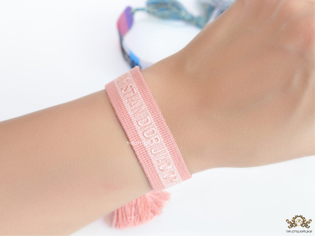 Adjustable pastel pink woven bracelet with knitted alphabets and tassels