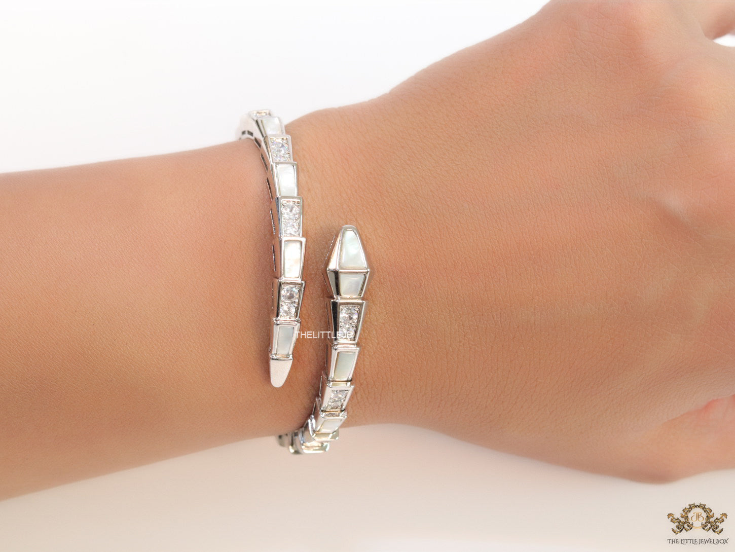 Open top platinum plated minimal serpentine bracelet with cubic zirconia stones and pearl white stones.