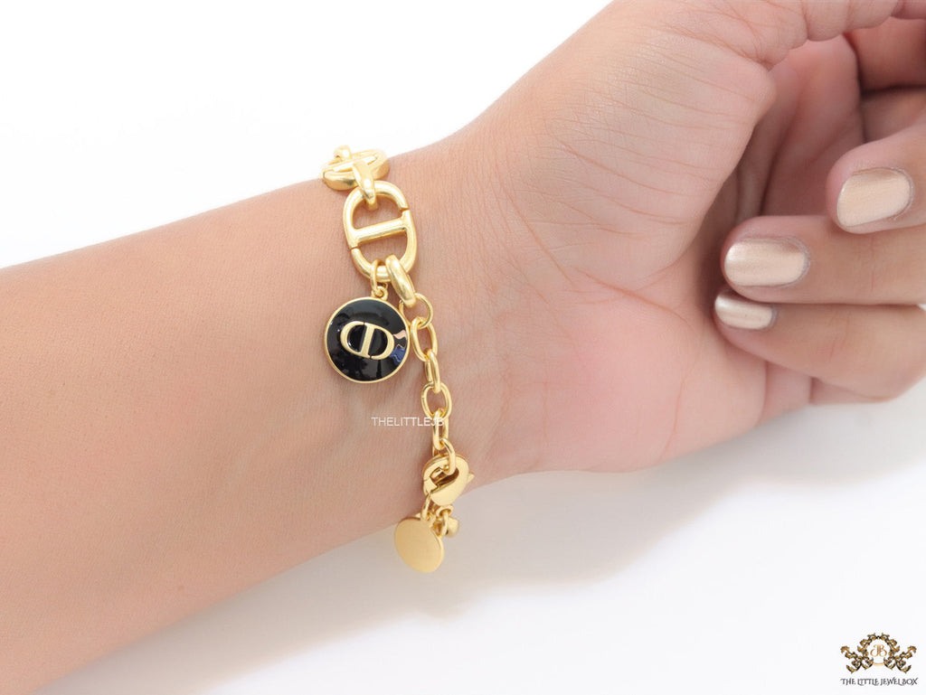 Gold plated link chain bracelet with charms, trinkets and black enamel charm with alphabets