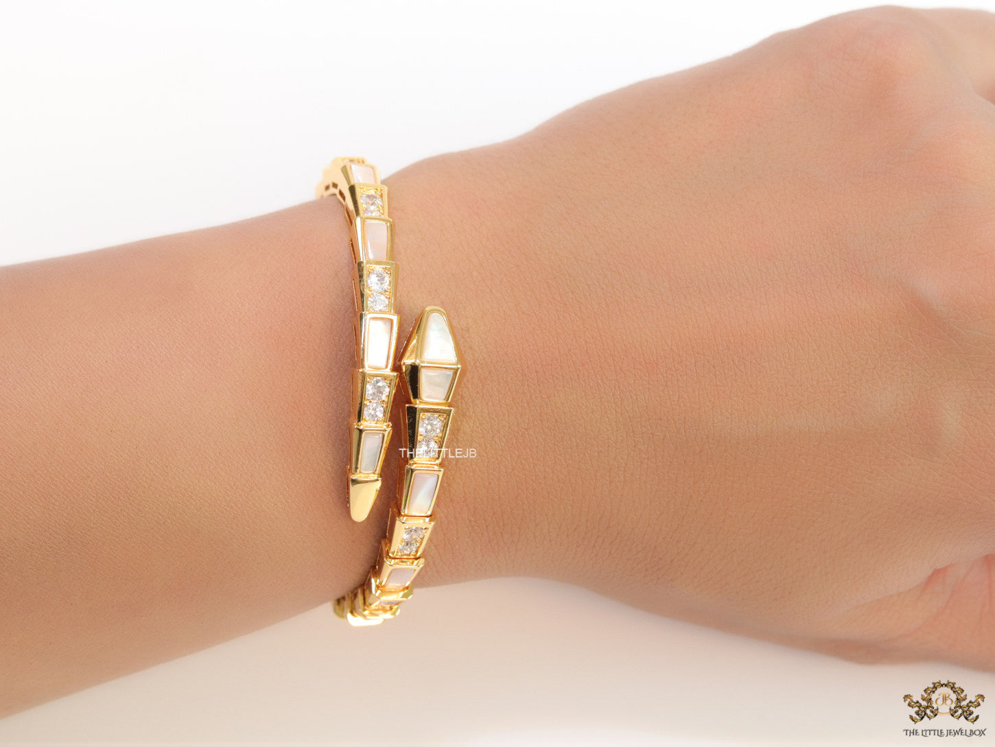 Open top gold plated minimal serpentine bracelet with cubic zirconia stones and pearl white stones.